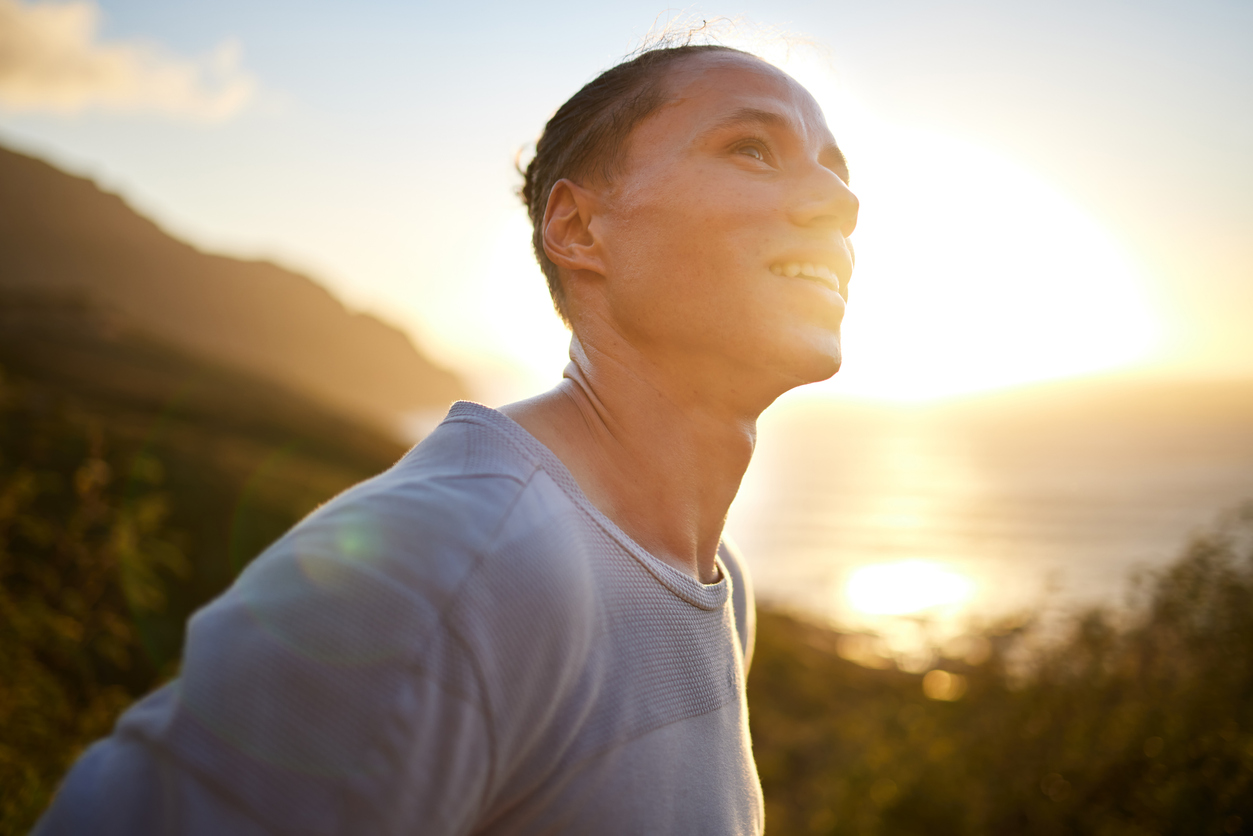 Individual staring hopefully upward surrounded by mountains, backlit from the sun.