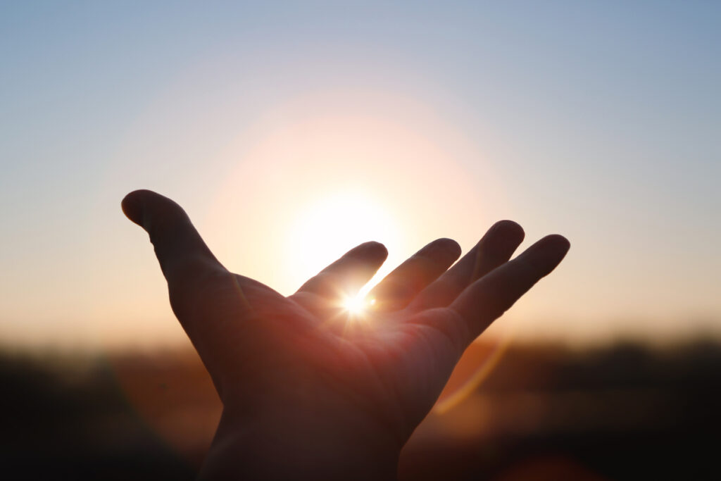 An open hand outstretched towards the sky with the sun visible through the fingers