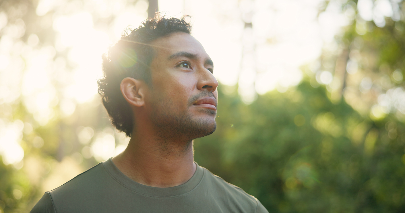 Man in nature hopefully looking up, backlit by the sun