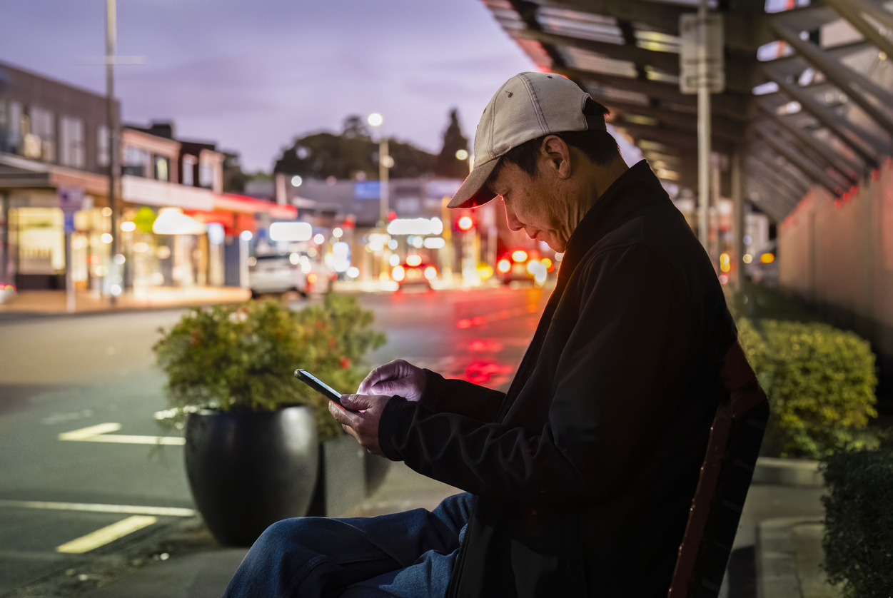 Man waiting for bus while checking his smartphone