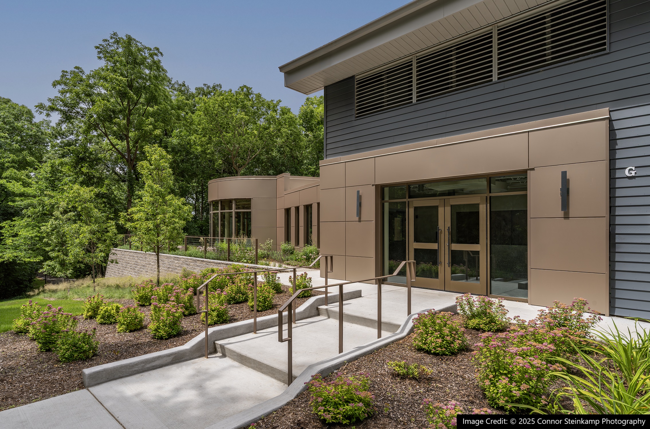 Entry lined with greenery to a building with large